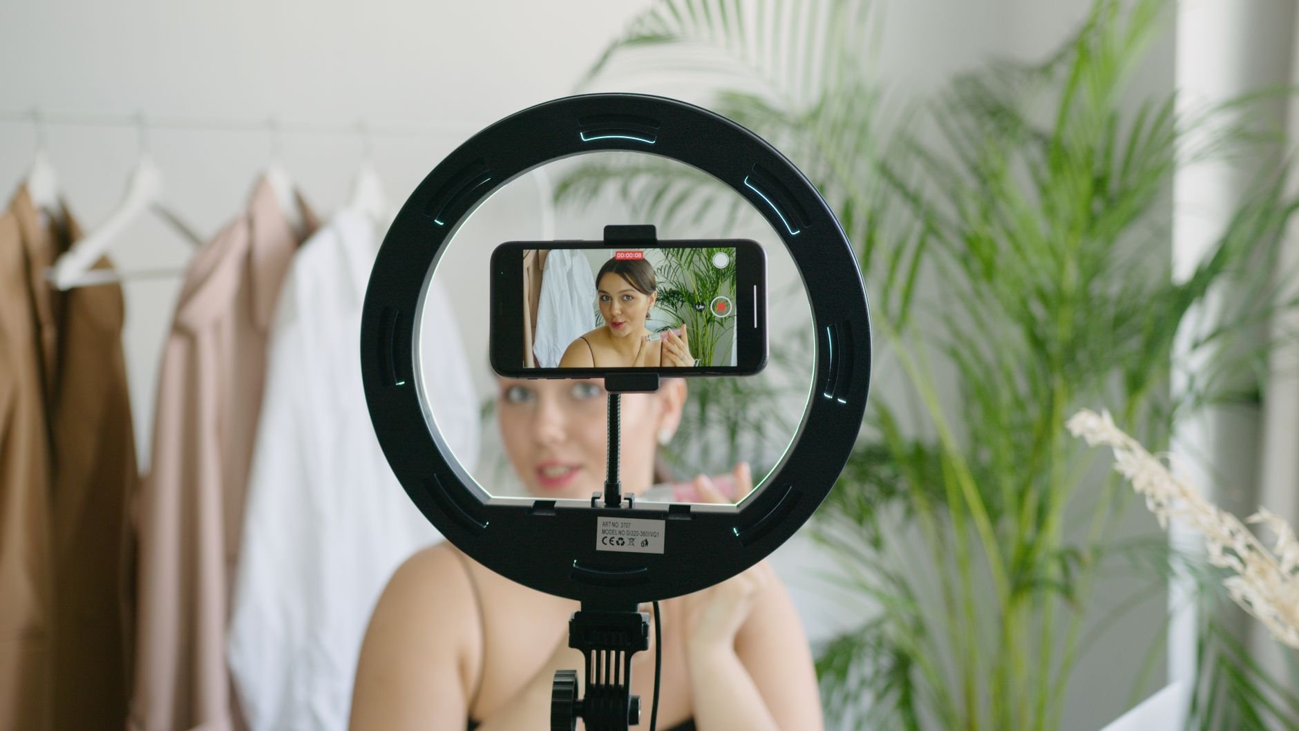 Woman creating video content using smartphone and ring light setup indoors.